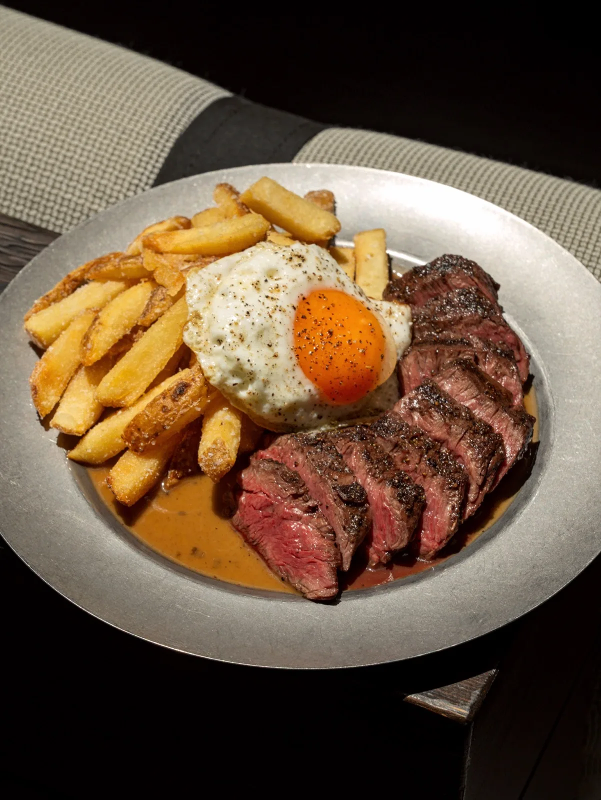 Sliced steak with fries and a fried egg on a pewter plate