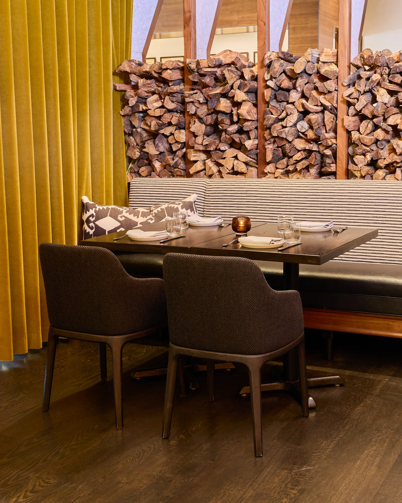 A banquette table in the private dining room, set beneath the stacked firewood wall