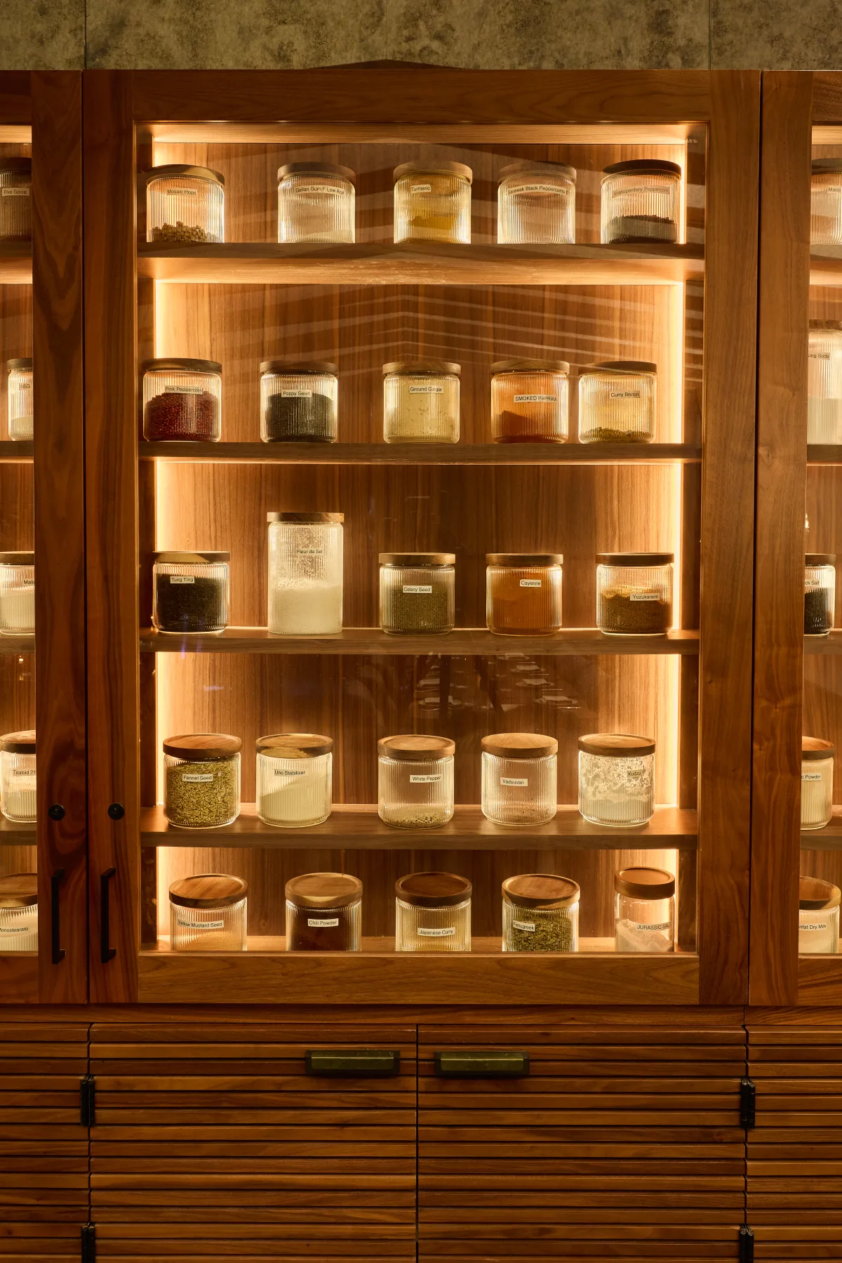 The lit pantry cabinet in the private dining room, filled with labelled jars of preserves and spices