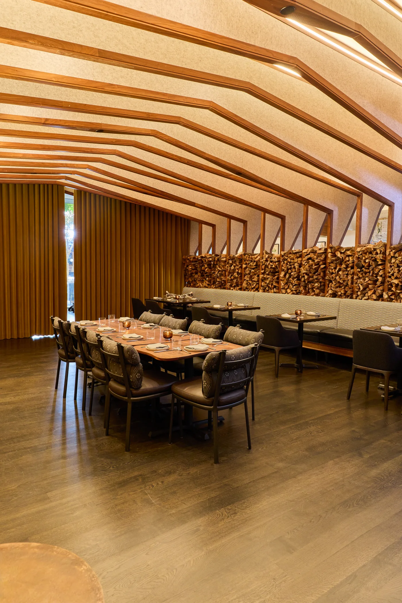 The private dining room at Darling, a long table under vaulted timber ribs beside the stacked firewood wall